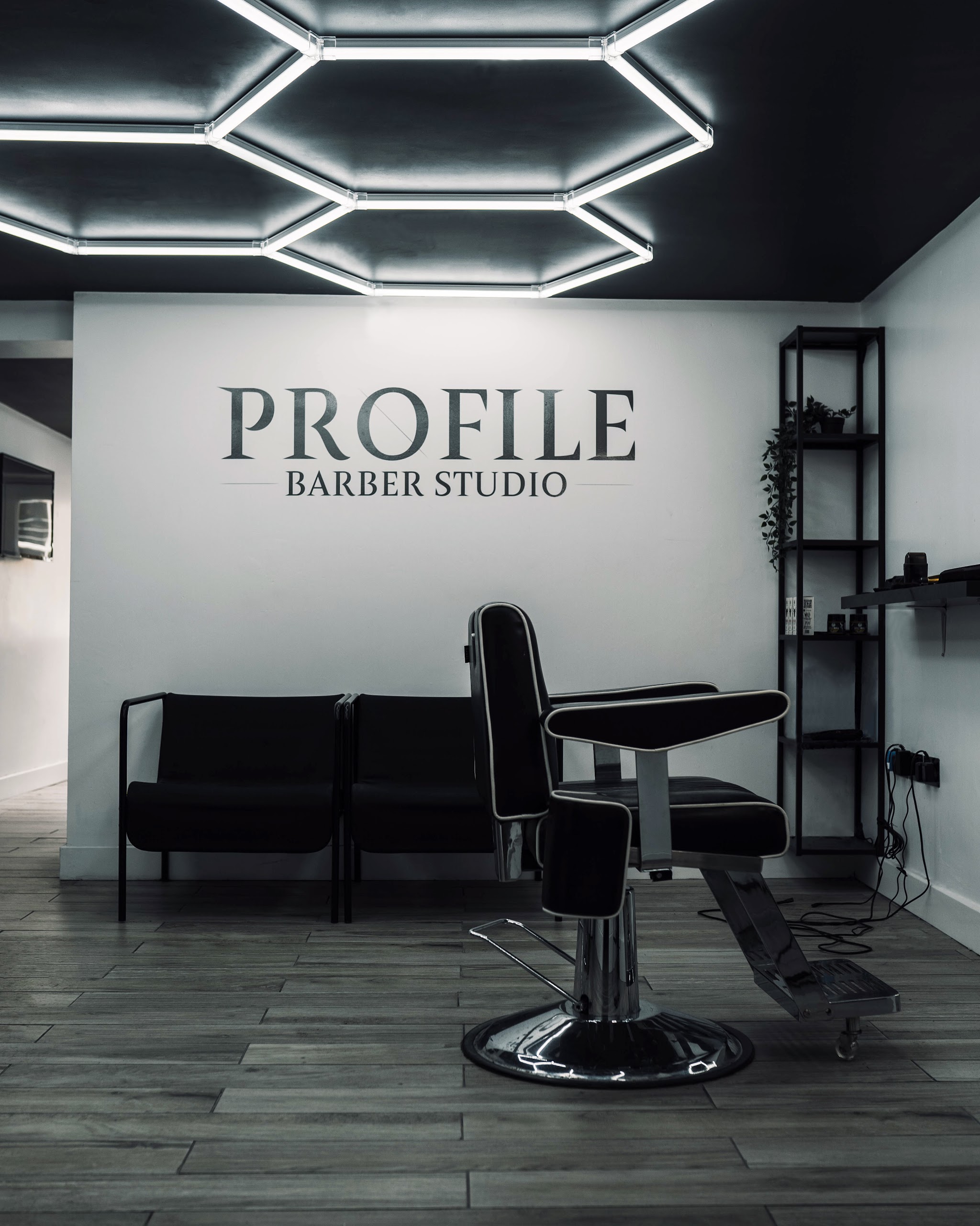 The empty studio: a barber's chair, waiting seats and the Profile Barber Studio sign under the hexagon lights