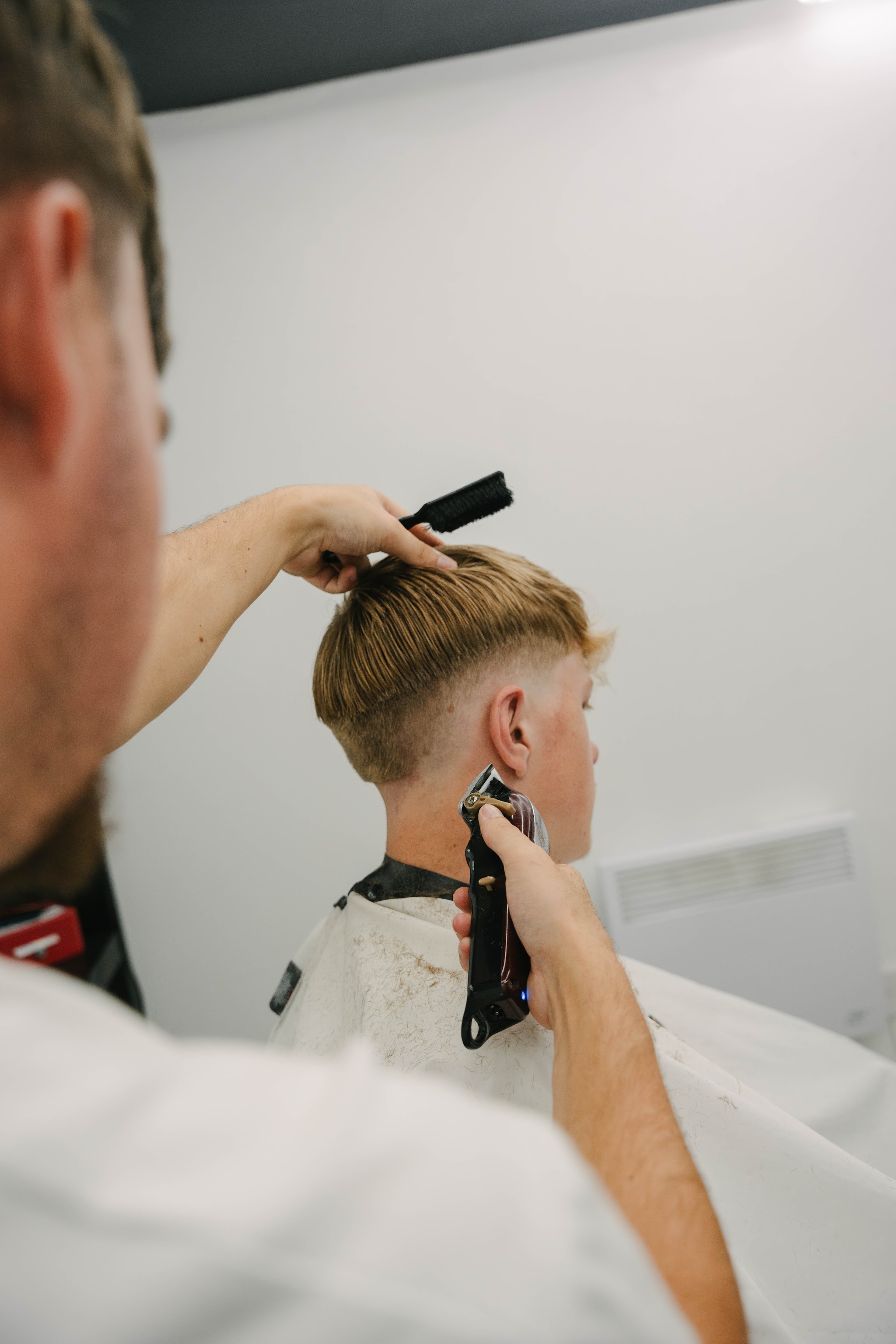A clipper fade in progress, comb held up through the hair
