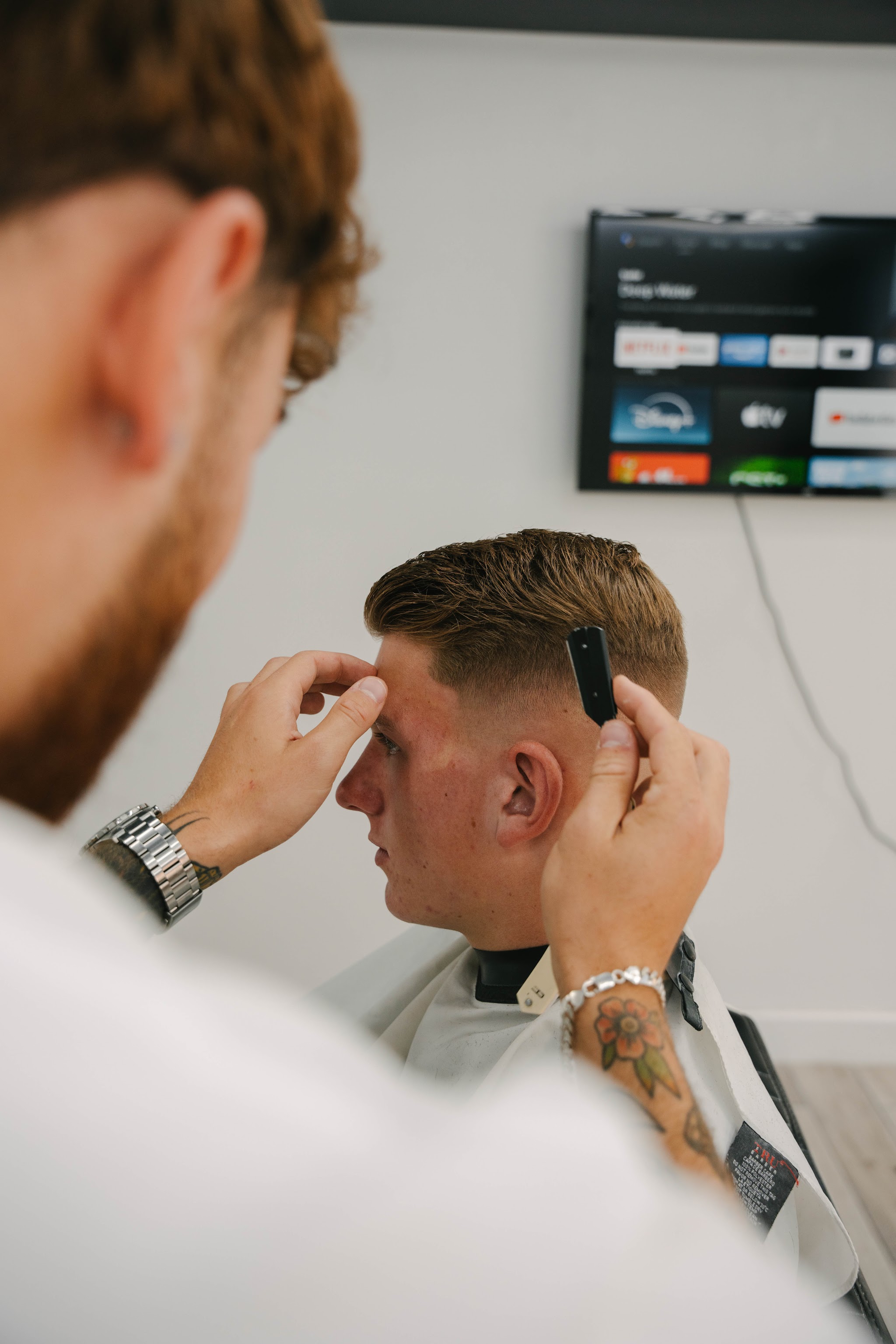 A barber styling the front of a client's hair, TV on the wall