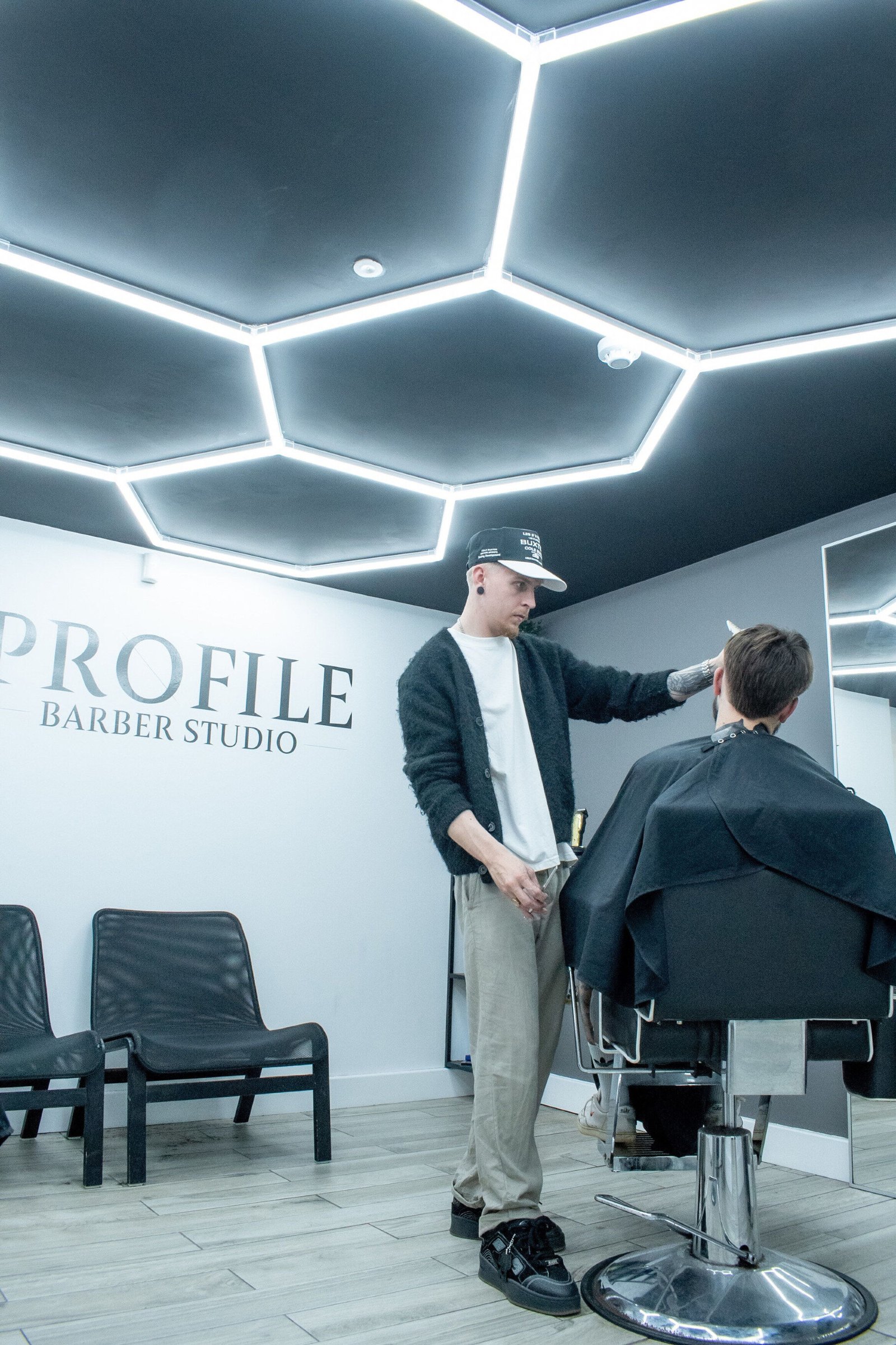 A barber at work under the hexagon LED ceiling, the Profile sign on the wall