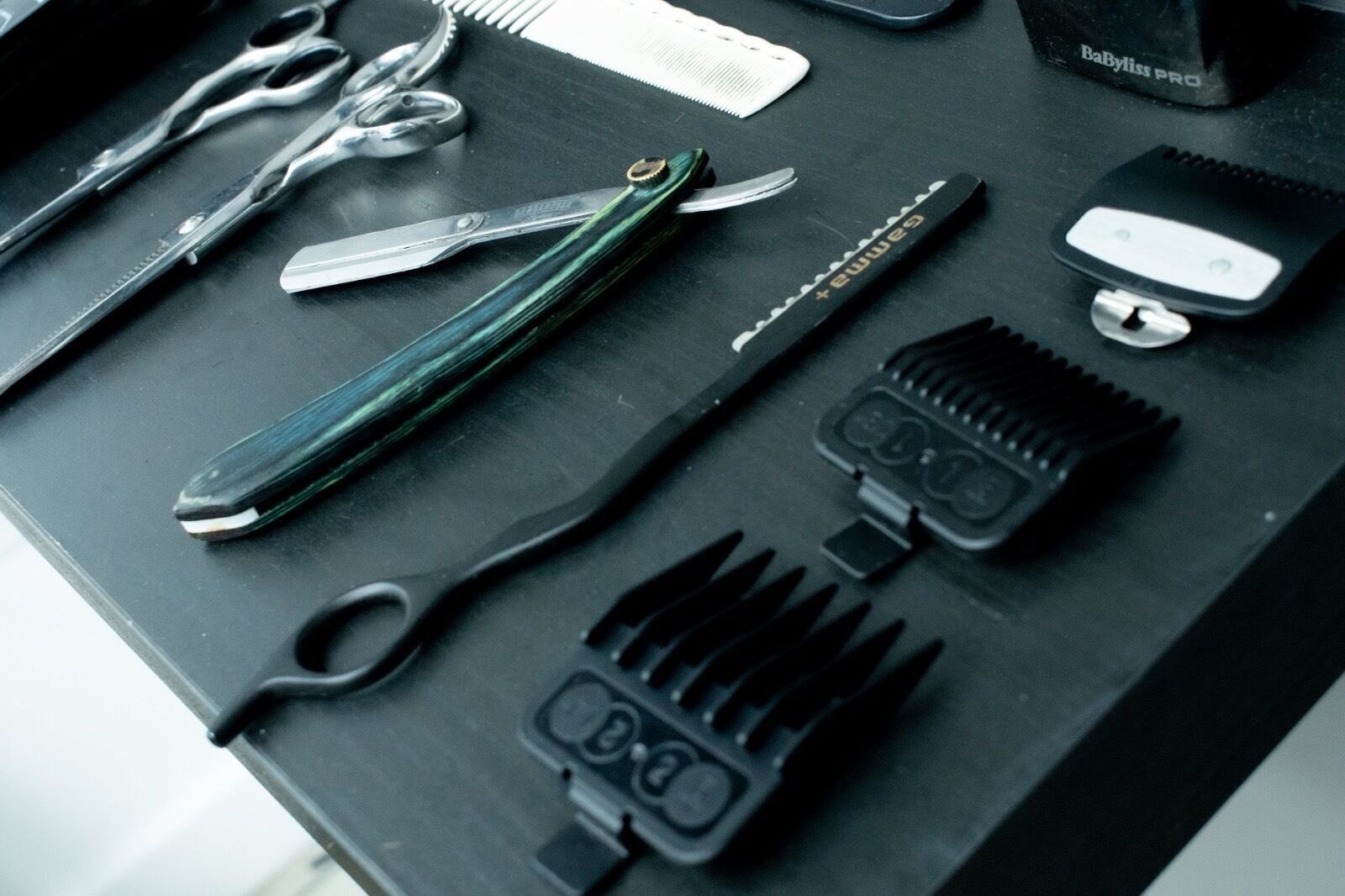 Scissors, a cut-throat razor and clipper guards laid out on a black worktop