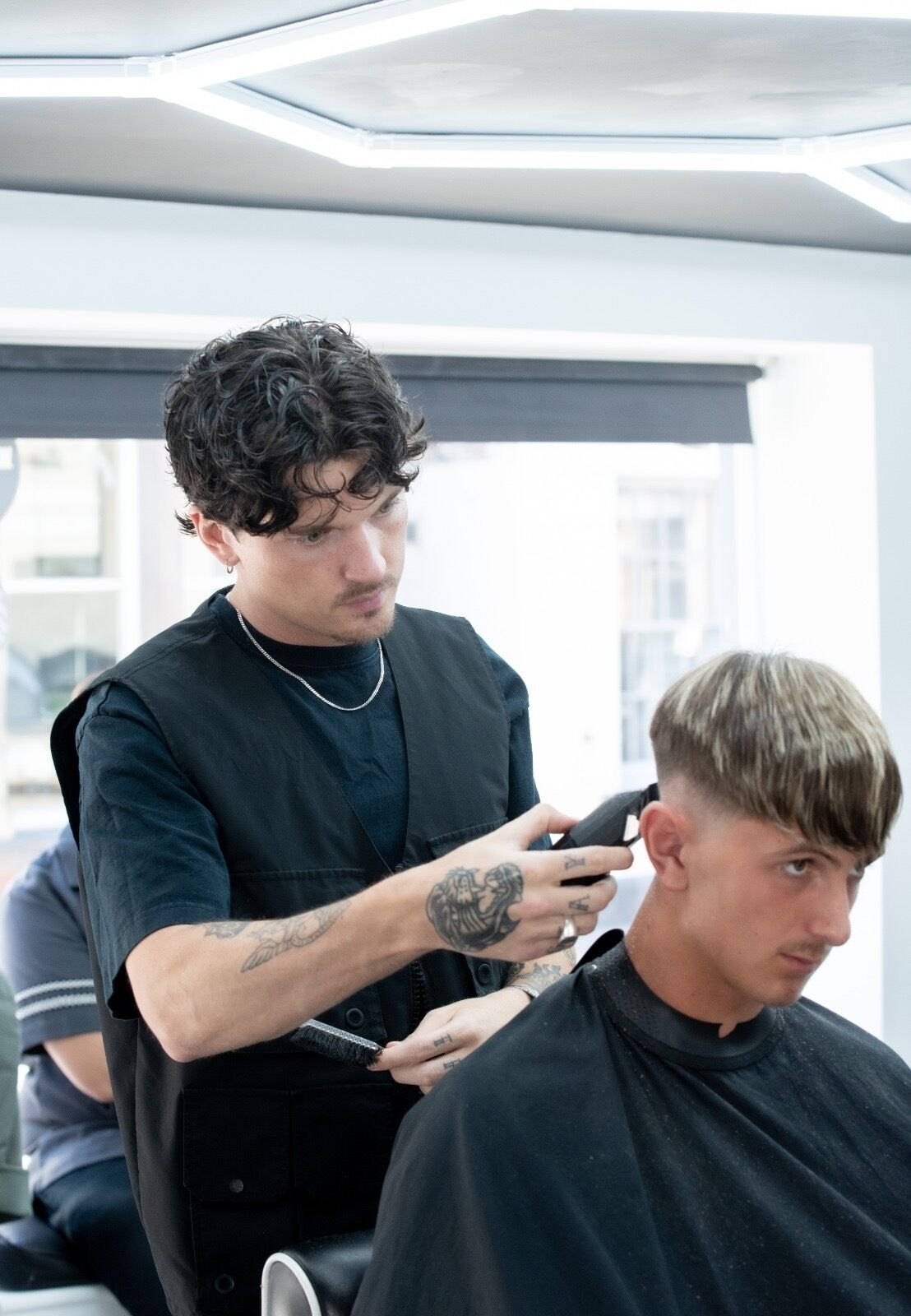 A barber clipper-cutting a client's hair under the LED ceiling