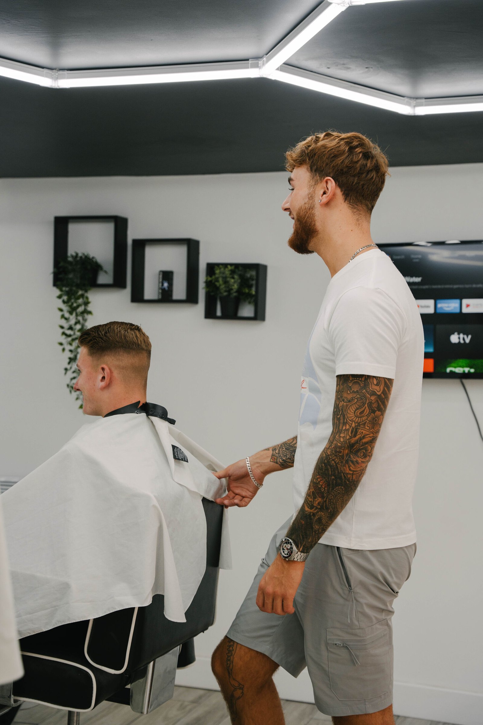 A barber checking a client's cut, shelves and plants on the wall behind
