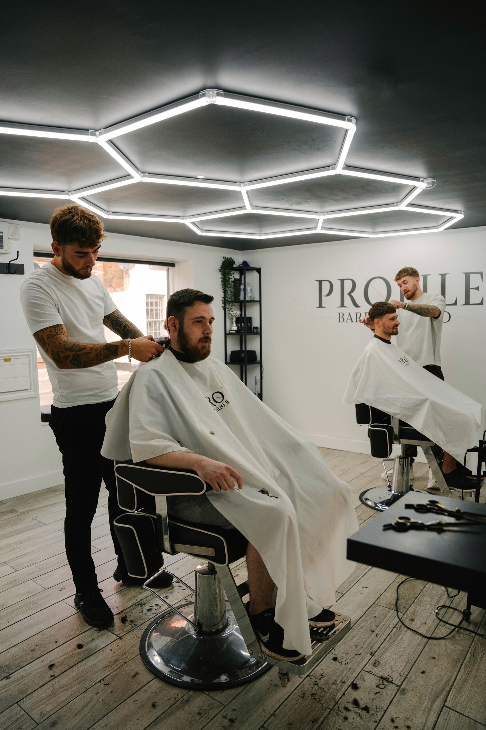 Inside Profile Barber Studio: two barbers at work under the hexagon LED ceiling, Profile sign on the back wall