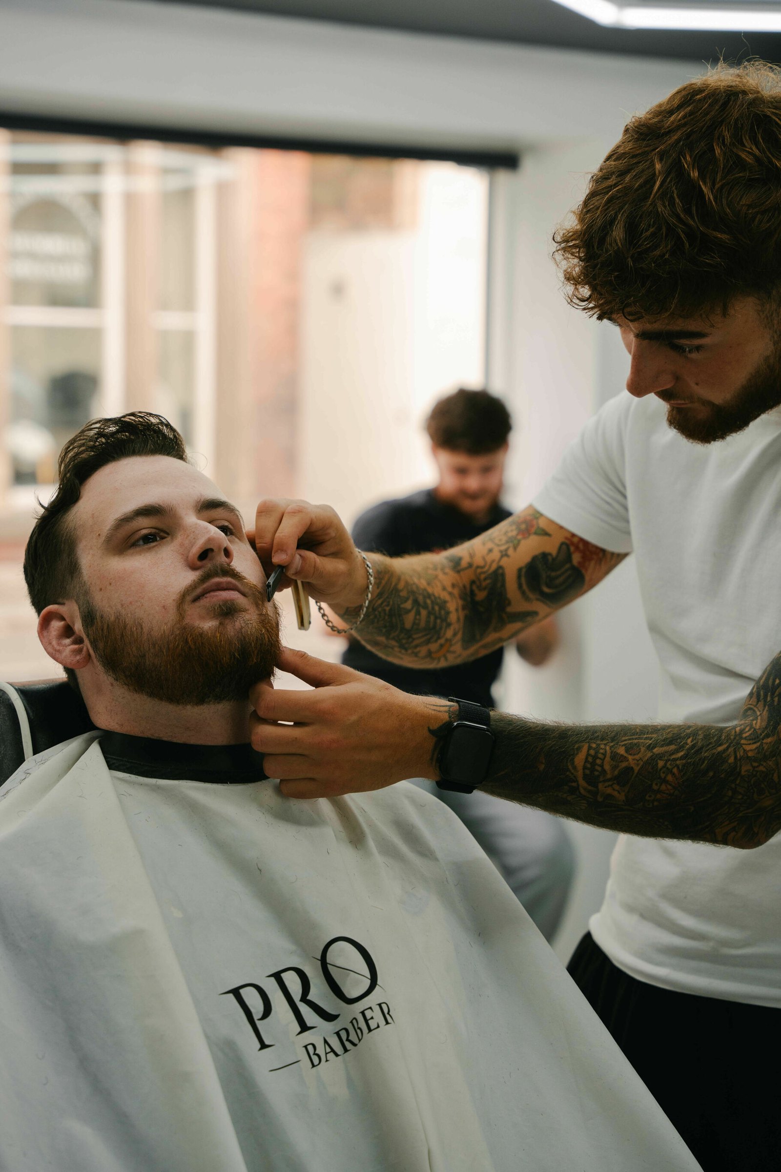 A beard being shaped, the client wearing a white Profile Barber gown
