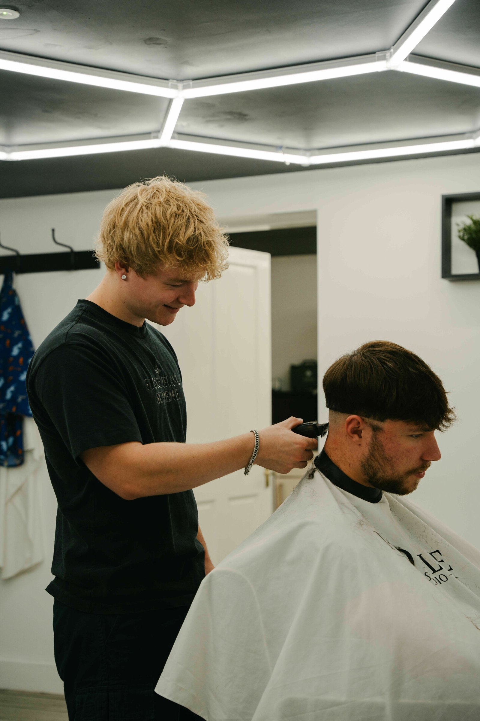 A barber working with clippers on a client in a Profile gown