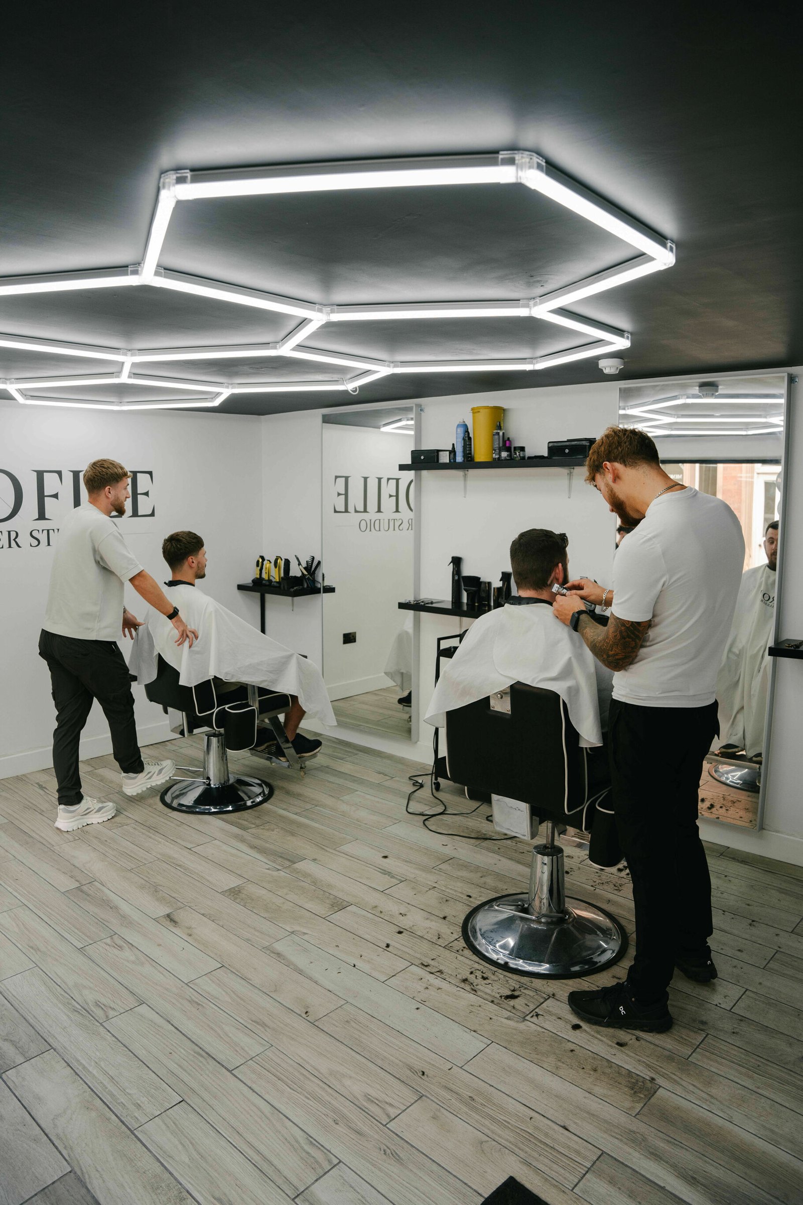 Two barbers at work under the hexagon LED ceiling, Profile sign on the wall