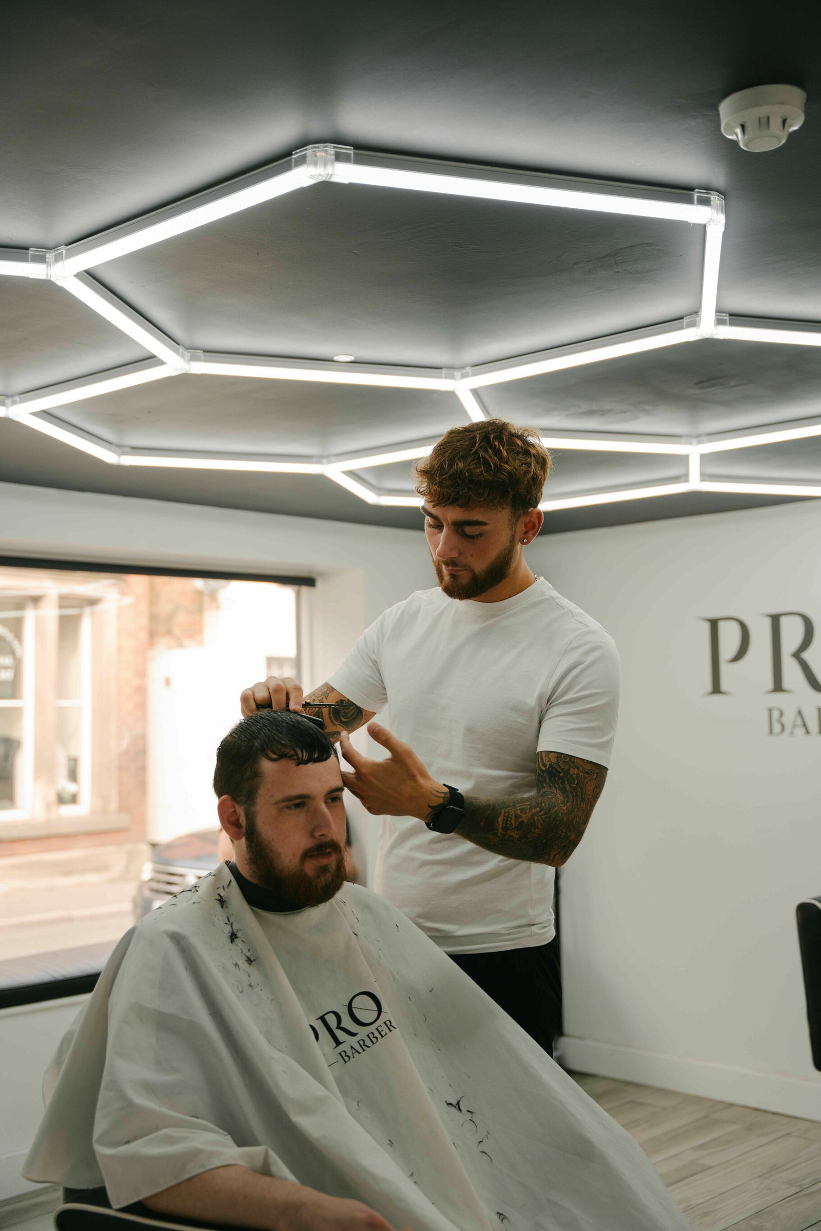A barber styling a client's hair beneath the glowing hexagon lights