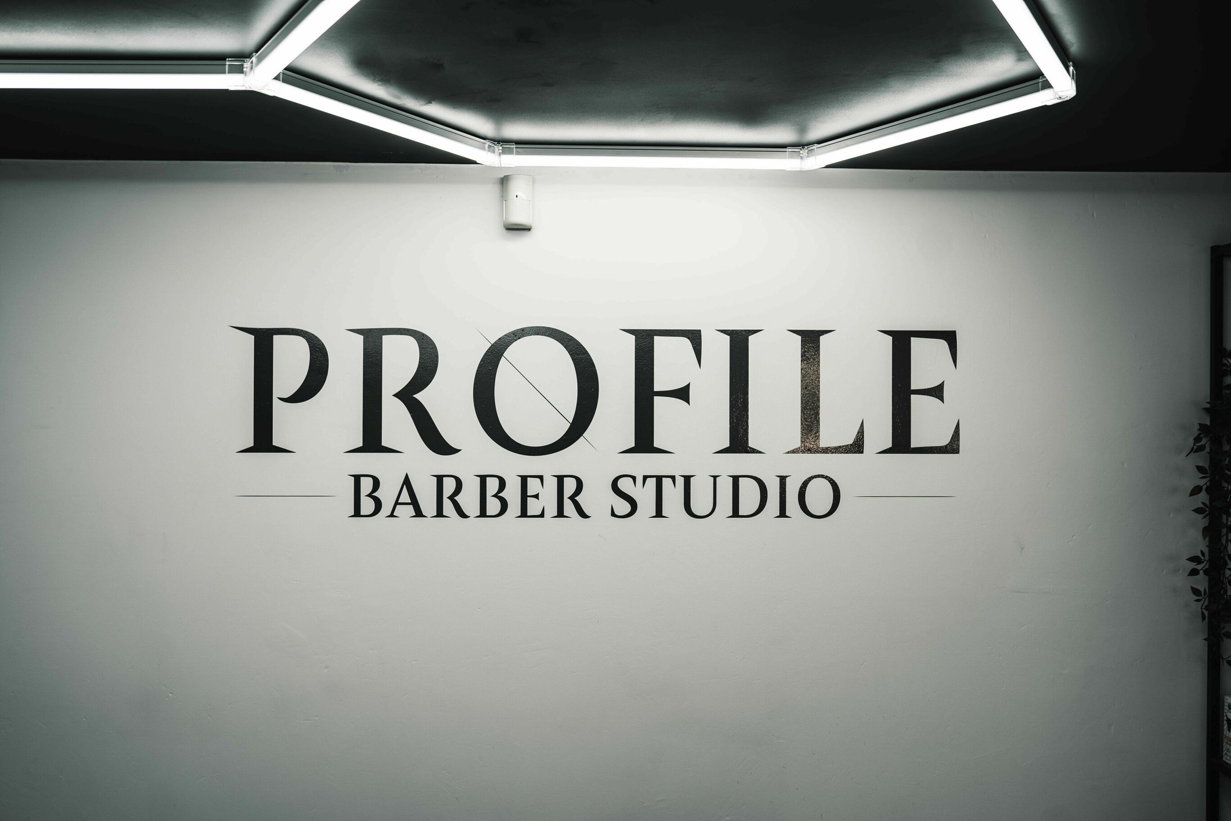 The Profile Barber Studio wall sign lit by the hexagon ceiling lights
